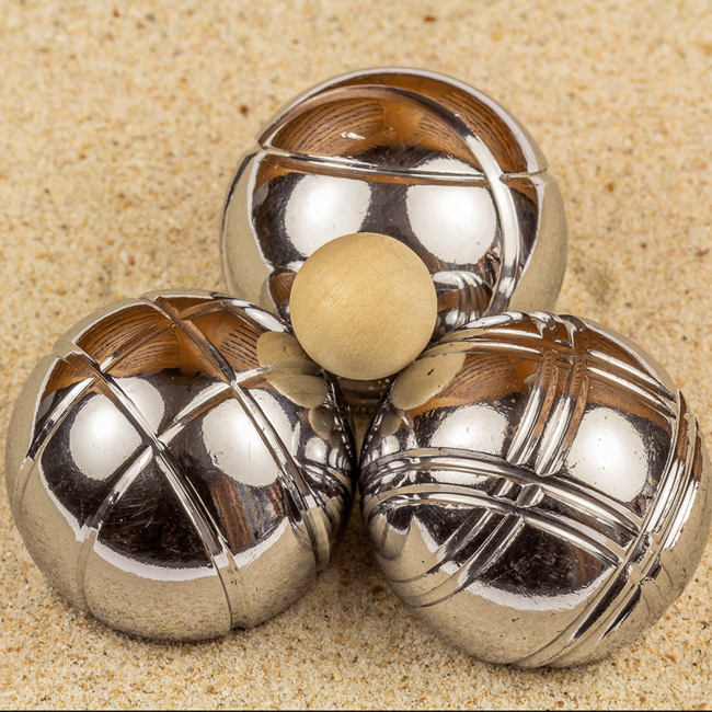 Drei große metallerne Petanque-Kugeln, die in einem Dreieck liegen. Auf ihnen liegt eine kleine hölzerne Kugel.