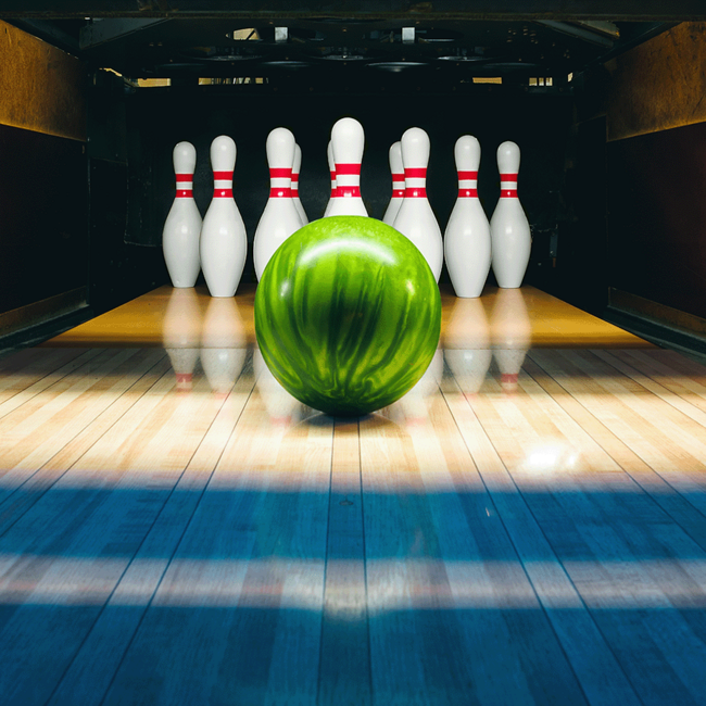 Eine Bowlingbahn auf der gerade eine grüne Bowlingkugel auf die Pins zurollt.