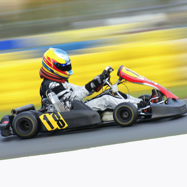 Eine Person sitzt in einem Go Kart mit der Nummer 18 vor einem verschwommenen gelb-blauen Hintergrund.